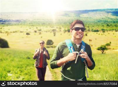 travel, tourism and people concept - happy couple with backpacks walking along country road over african savannah background. happy couple with backpacks traveling in africa. happy couple with backpacks traveling in africa