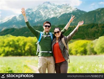 travel, tourism and people concept - happy couple with backpacks waving hands over mountains background. happy couple with backpacks hiking outdoors