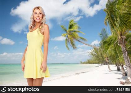 travel, tourism and people concept - happy smiling beautiful young woman in yellow dress over exotic tropical beach with palm trees background. happy young woman over exotic tropical beach
