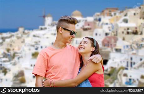 travel, tourism and people concept - happy smiling teenage couple hugging and looking at each other over oia town on santorini island background. happy teenage couple on santorini island