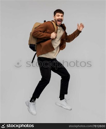 travel, tourism and people concept - happy smiling young man with backpack jumping in air over grey background. smiling young man with backpack jumping in air