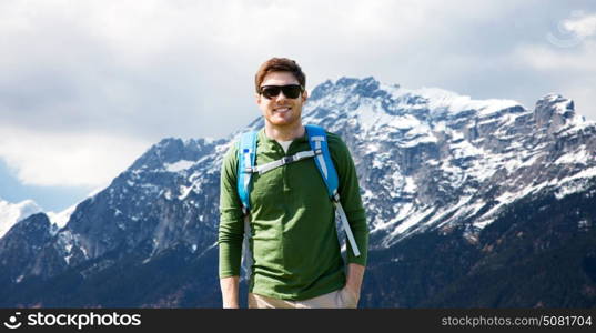 travel, tourism and people concept - happy young man in sunglasses with backpack over alps mountains background. happy man with backpack traveling in highlands