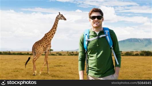 travel, tourism and people concept - happy young man in sunglasses with backpack over african savannah and giraffe background. happy young man with backpack traveling in africa. happy young man with backpack traveling in africa