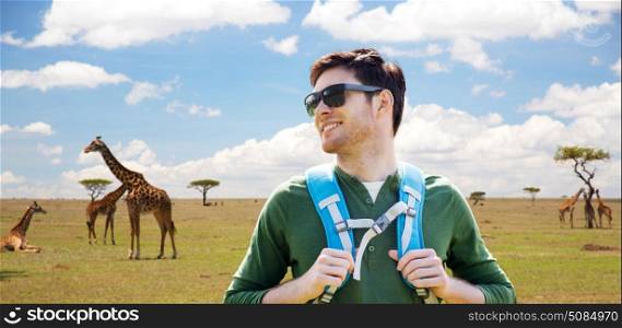 travel, tourism and people concept - happy young man in sunglasses with backpack traveling over african savannah and giraffes background. happy young man with backpack traveling in africa. happy young man with backpack traveling in africa