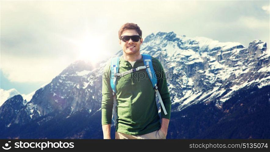 travel, tourism and people concept - happy young man in sunglasses with backpack over alps mountains background. happy man with backpack traveling in highlands. happy man with backpack traveling in highlands