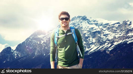 travel, tourism and people concept - happy young man in sunglasses with backpack over alps mountains background. happy man with backpack traveling in highlands. happy man with backpack traveling in highlands