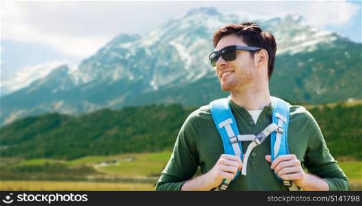 travel, tourism and people concept - happy young man in sunglasses with backpack traveling over alps mountains background. happy man with backpack traveling in highlands