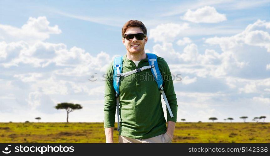 travel, tourism and people concept - happy young man in sunglasses with backpack over african savannah background. happy young man with backpack traveling in africa