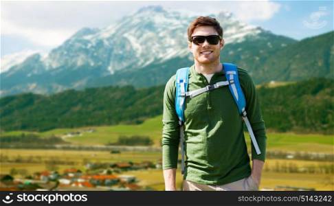 travel, tourism and people concept - happy young man in sunglasses with backpack over alps mountains background. happy man with backpack traveling in highlands