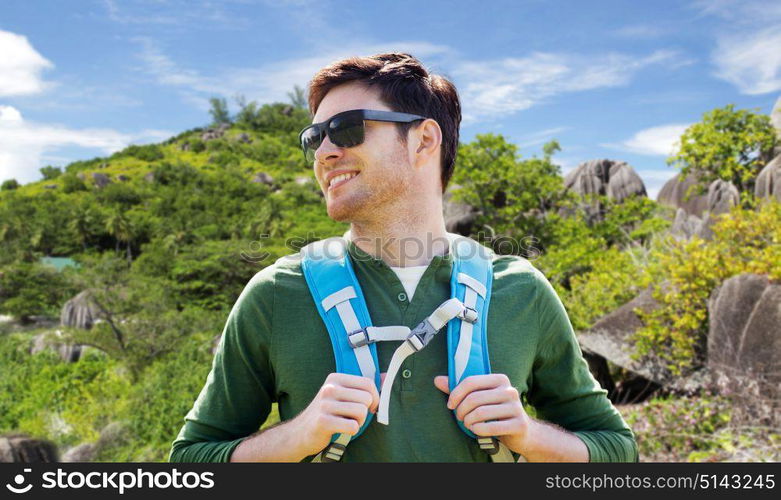 travel, tourism and people concept - happy young man in sunglasses with backpack traveling over exotic island hills background. happy man with backpack traveling over island