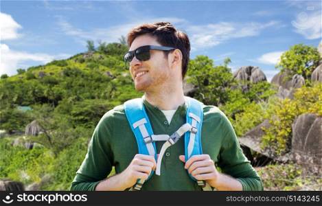 travel, tourism and people concept - happy young man in sunglasses with backpack traveling over exotic island hills background. happy man with backpack traveling over island