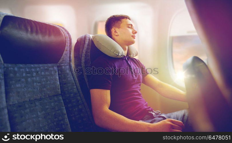 travel, tourism and people concept - happy young man sleeping in plane with inflatable pillow over porthole background. young man sleeping in plane with travel pillow. young man sleeping in plane with travel pillow
