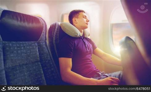 travel, tourism and people concept - happy young man sleeping in plane with inflatable pillow over porthole background. young man sleeping in plane with travel pillow. young man sleeping in plane with travel pillow