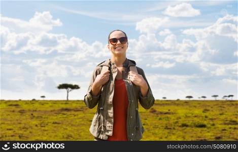 travel, tourism and people concept - happy young woman in sunglasses with backpack over african savannah background. happy woman with backpack traveling in africa