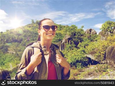 travel, tourism and people concept - happy young woman in sunglasses with backpack over natural exotic island background. happy young woman with backpack traveling