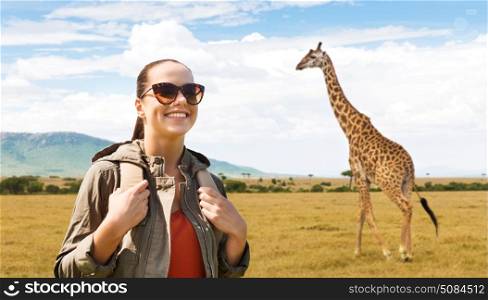 travel, tourism and people concept - happy young woman in sunglasses with backpack over african savannah and giraffe background. happy woman with backpack traveling in africa. happy woman with backpack traveling in africa