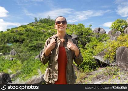 travel, tourism and people concept - happy young woman in sunglasses with backpack over natural exotic island background. happy young woman with backpack traveling. happy young woman with backpack traveling