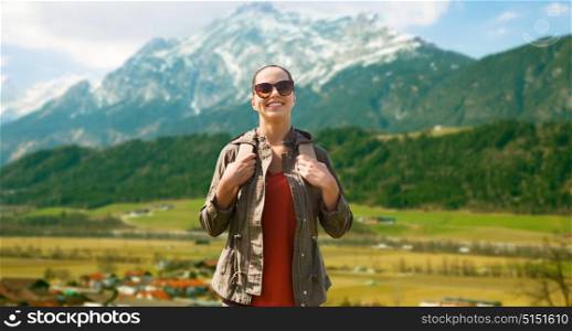 travel, tourism and people concept - happy young woman in sunglasses with backpack traveling over mountains background. happy woman with backpack traveling in highlands