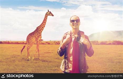 travel, tourism and people concept - happy young woman in sunglasses with backpack over african savannah and giraffe background. happy woman with backpack traveling in africa