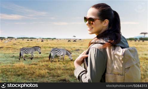 travel, tourism and people concept - happy young woman with backpack over african savannah and zebras background. happy woman with backpack traveling in africa. happy woman with backpack traveling in africa