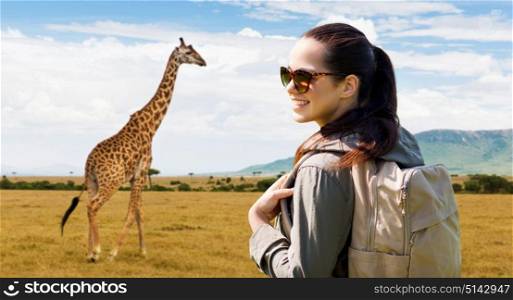 travel, tourism and people concept - happy young woman with backpack over african savannah and giraffe background. happy woman with backpack traveling in africa