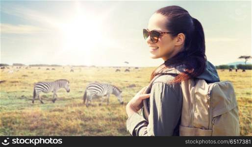 travel, tourism and people concept - happy young woman with backpack over african savannah and zebras background. happy woman with backpack traveling in africa. happy woman with backpack traveling in africa