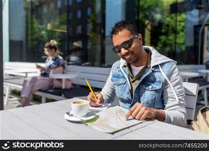 travel, tourism and people concept - indian man with map, notebook and coffee at street cafe in city. man with map and notebook at street cafe in city