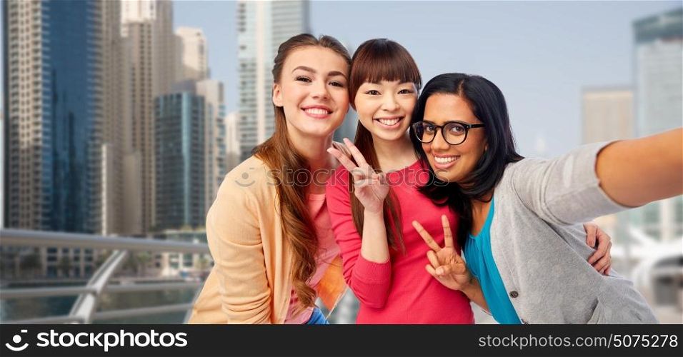 travel, tourism and people concept - international group of happy smiling different women taking selfie and showing peace hand sign over dubai city street background. international happy women taking selfie in city