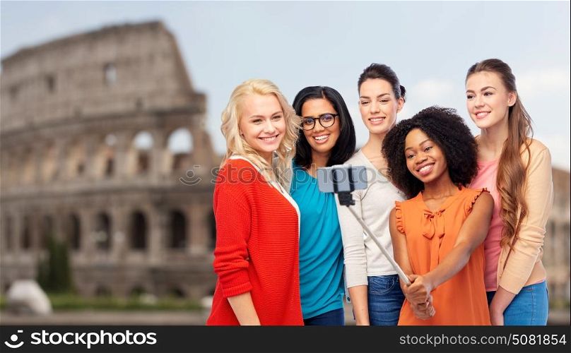 travel, tourism and people concept - international group of happy smiling different women taking picture with smartphone on selfie stick over coliseum background. international women taking selfie over coliseum