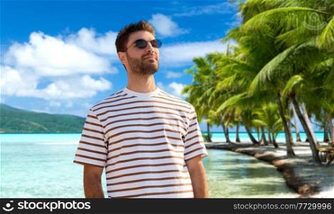 travel, tourism and people concept - portrait of young man in sunglasses over tropical beach background in french polynesia. young man in sunglasses on tropical beach