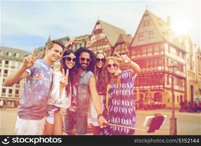 travel, tourism and people concept - smiling young hippie friends in sunglasses taking picture by smartphone selfie stick and showing peace sign over frankfurt am main city street background. happy hippie friends taking selfie in frankfurt
