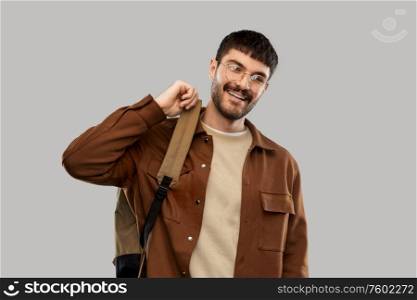 travel, tourism and people concept - smiling young man in glasses with backpack over grey background. smiling young man in glasses with backpack