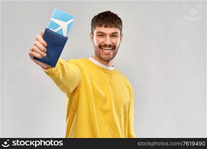 travel, tourism and people concept - smiling young man in yellow sweatshirt with air ticket and passport over grey background. smiling young man with air ticket and passport