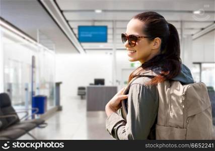 travel, tourism and people concept - smiling young woman in sunglasses with backpack over airport terminal background. young woman with backpack over airport terminal