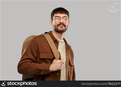 travel, tourism and people concept - young man in glasses with backpack over grey background. young man in glasses with backpack