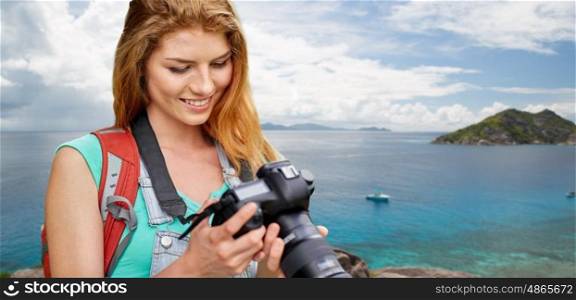 travel, tourism and photography concept - happy young woman with backpack and camera photographing over background of seychelles island in indian ocean. woman with backpack and camera over beach