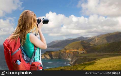 travel, tourism and photography concept - happy young woman with backpack and camera photographing over bixby creek bridge on big sur coast of california background. woman with backpack and camera at big sur coast. woman with backpack and camera at big sur coast