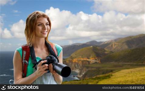 travel, tourism and photography concept - happy young woman with backpack and camera photographing over bixby creek bridge on big sur coast of california background. woman with backpack and camera at big sur coast. woman with backpack and camera at big sur coast