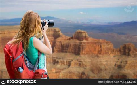 travel, tourism and photography concept - happy young woman with backpack and camera photographing over grand canyon national park background. woman with backpack and camera at grand canyon