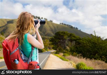 travel, tourism and photography concept - happy young woman with backpack and camera photographing over big sur hills of california background. woman with backpack and camera at big sur coast. woman with backpack and camera at big sur coast
