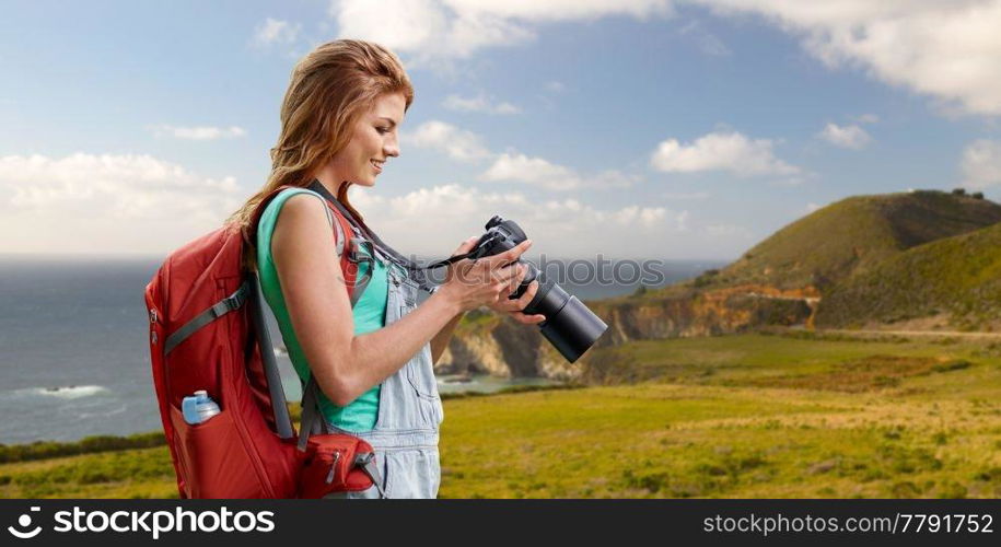 travel, tourism and photography concept - happy young woman with backpack and camera photographing over big sur coast of california background. woman with backpack and camera at big sur coast