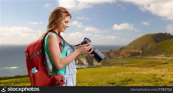 travel, tourism and photography concept - happy young woman with backpack and camera photographing over big sur coast of california background. woman with backpack and camera at big sur coast