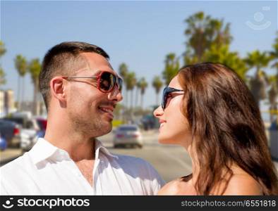 travel, tourism and relationships concept - happy smiling couple in sunglasses hugging over venice beach background in california. happy couple in sunglasses over venice beach. happy couple in sunglasses over venice beach
