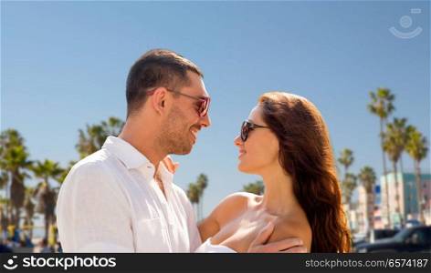 travel, tourism and relationships concept - happy smiling couple in sunglasses hugging over venice beach background in california. happy couple in sunglasses over venice beach