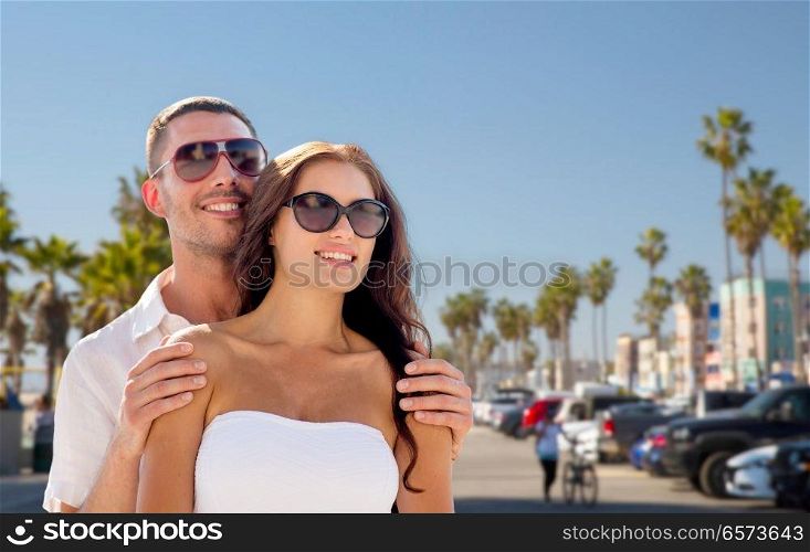 travel, tourism and relationships concept - happy smiling couple in sunglasses over venice beach background in california. happy couple in sunglasses over venice beach