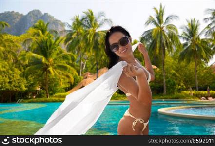 travel, tourism and summer concept - happy smiling young woman in bikini swimsuit with cover-up over swimming pool and palms on background. woman in bikini swimsuit with cover-up on beach