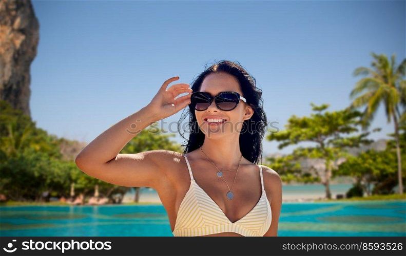 travel, tourism and summer concept - happy smiling young woman in sunglasses and bikini swimsuit over bali beach background. smiling young woman in sunglasses on summer beach