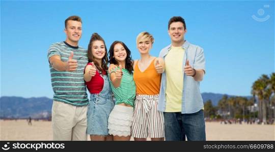 travel, tourism and summer holidays concept - group of happy smiling friends hugging showing thumbs up over venice beach background in california. happy friends showing thumbs up over venice beach