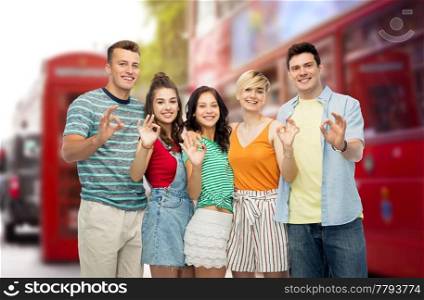 travel, tourism and summer holidays concept - group of happy smiling friends showing ok hand sign over london city street background. happy friends showing ok over london city street