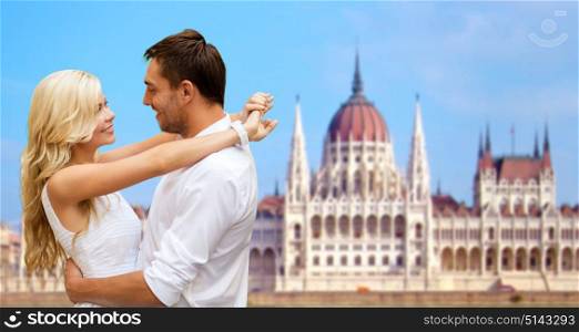 travel, tourism and summer holidays concept - happy couple hugging over house of parliament in budapest background. happy couple over house of parliament in budapest